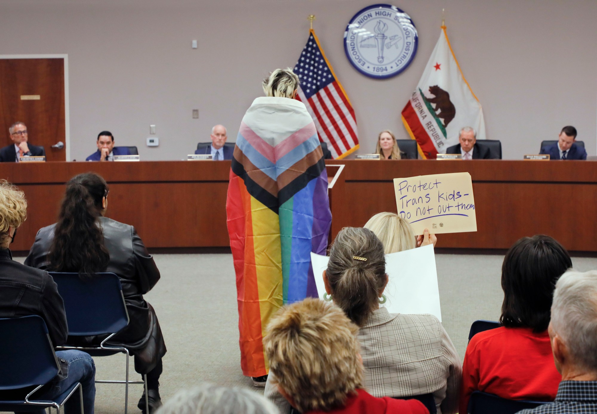 A teacher's aide wrapped in a Pride flag speaks at a school board meeting about gender disclosure policies