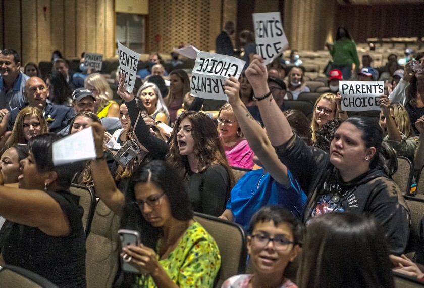 People hold signs and chant during a meeting of the North Allegheny School District school board regarding the district's mask policy, at at North Allegheny Senior High School in McCandless, Pa., on Aug. 25, 2021. A growing number of school board members across the U.S. are resigning or questioning their willingness to serve as meetings have devolved into shouting contests over contentious issues including masks in schools.