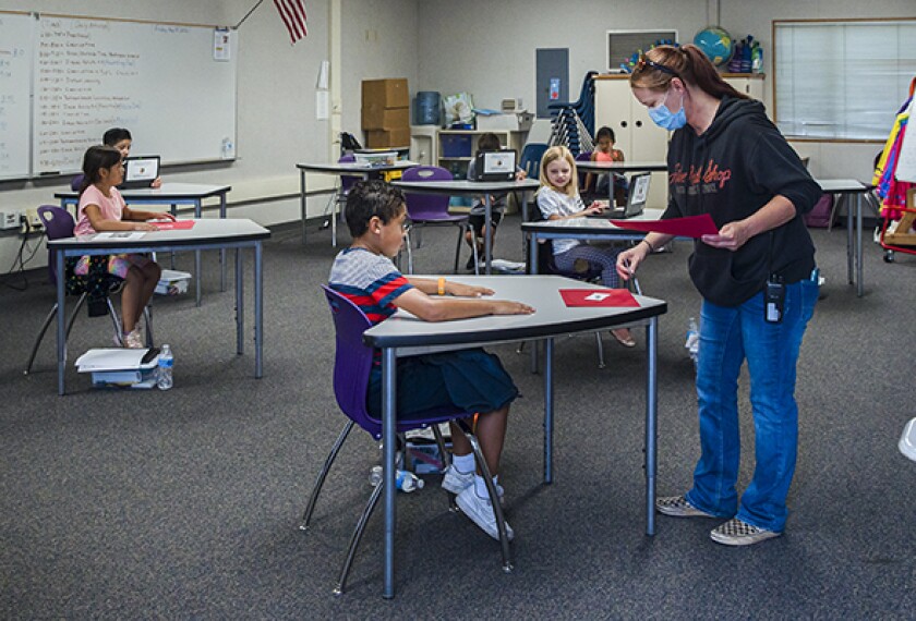 Teacher Danielle Elliot wears a face mask while speaking to Hayden A. while Rayonna A., Lauren T., Alice C. and Luciano M. sit at an appropriate social distance during an arts and crafts class at Chase Avenue School in El Cajon, Calif.