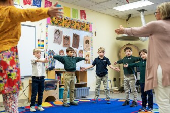 First graders begin their art class with fine and gross motor warmups lead by art teacher Kesling St. Denis, left, on March 30, 2023.