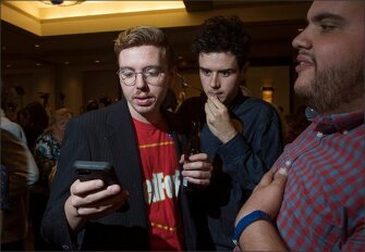Arizona teachers Nicholas Martin, 25, from left, Noah Karvelis, 24, and Jay Barbuto, 29, all from Phoenix, look at election results during the Arizona Democrats election watch party on Nov. 6 in Phoenix, Ariz.
