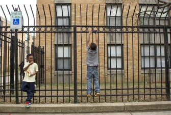 Dashawn Smith, 6, left, looks over at his friend Malachi Davis, 10, as he hangs off of a fence outside of their apartment building while waiting for a bus to an after-care program. District of Columbia officials erected a prison-grade iron fence around the Potomac Gardens public housing complex in the early 1990s to keep out drug dealers and other criminals. At the time, the fence stirred an emotional reaction from residents, who said it made them feel further separated from the surrounding neighborhood.