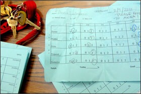 Paraprofessional Alisa Minar’s desk is littered with blue performance reports for Andro and other students prior to morning check-in at Sylvester Middle.