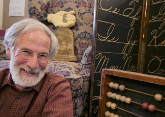 Educator and K-12 memorabilia collector Richard Lodish is surrounded by some of the items at his home in Bethesda, Md. An old wooden school bell, at left, dates from the early 19th century; a D’nealian cursive handwriting chart is at center, and an oversize abacus at right. –Charles Borst/Education Week