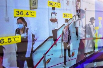 Students wearing protective face masks to help curb the spread of the new coronavirus are reflected on a monitor screen showing their body temperatures as they arrive at a high school in Wuhan in central China’s Hubei province, Wednesday, May 6, 2020.