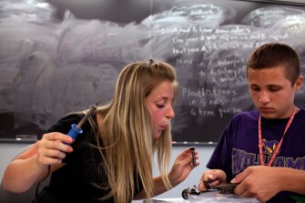 Teaching Assistant Haley Carpenter, left, helps Eric Simioni, 14, with soldering a solar-powered car in the Principles of Engineering Design class during Center for Talented Youth summer program.