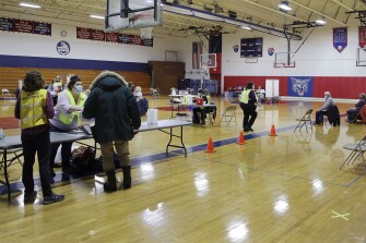 People wait for their turn to receive a COVID-19 vaccine, right, as public health experts with the Vermont Health Department begin vaccinating people aged 75 and older at the Hazen Union High School in Hardwick, Vt. on Jan. 27, 2021.
