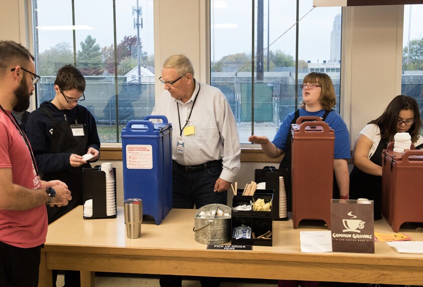 Special education teacher Chris Simley, left, places a coffee order at a table staffed by student Jon Hahn, volunteer Phil Tegeler, student Brianna Dewater and student Mykala Robinson at Common Grounds coffee shop at Lincoln High in Lincoln, Neb., on Oct. 26, 2018. Down a hallway lined with Lincoln High School's signature red lockers, through the doors of Room 123, teachers can find a little early-morning salvation: a caffeine oasis open for business each Friday morning.