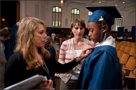 Liz Cox, left, an administrator at the Academy @ Shawnee, helps senior T’uana Hanley with her gown for the school's upcoming graduation day, as librarian Stephanie Conrad watches.