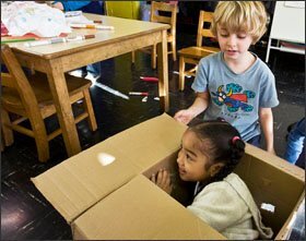 Drew Bolotsky, 5, helps Deja Martin, 4, into the “box house” he made from art materials during choice time.