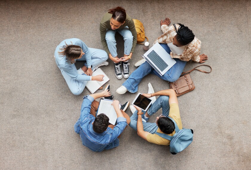 Image of teens sitting in a circle on the floor doing work and being social.