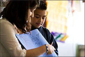 Arriba: La maestra, Talina Avila, ayuda Joshua Flores a hablar sobre el dibujo en la clase de jardín maternal en la Academia de Dos Idiomas, donde hay una mezcla de hablantes nativos de inglés y español.
