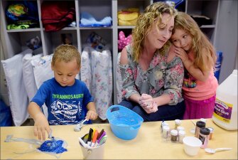 Lead teacher Melanie McLaughlin gets a hug from her student, Daleyza Gaona, 4, as Caidyn Smith, 4, works with “slime” in their classroom at Early Childhood Development Center Reed, a Head Start program in Tulsa, Okla. The center used statistical modeling to reduce the number of “no show” students from 38 in 2016 to 11 in 2017.