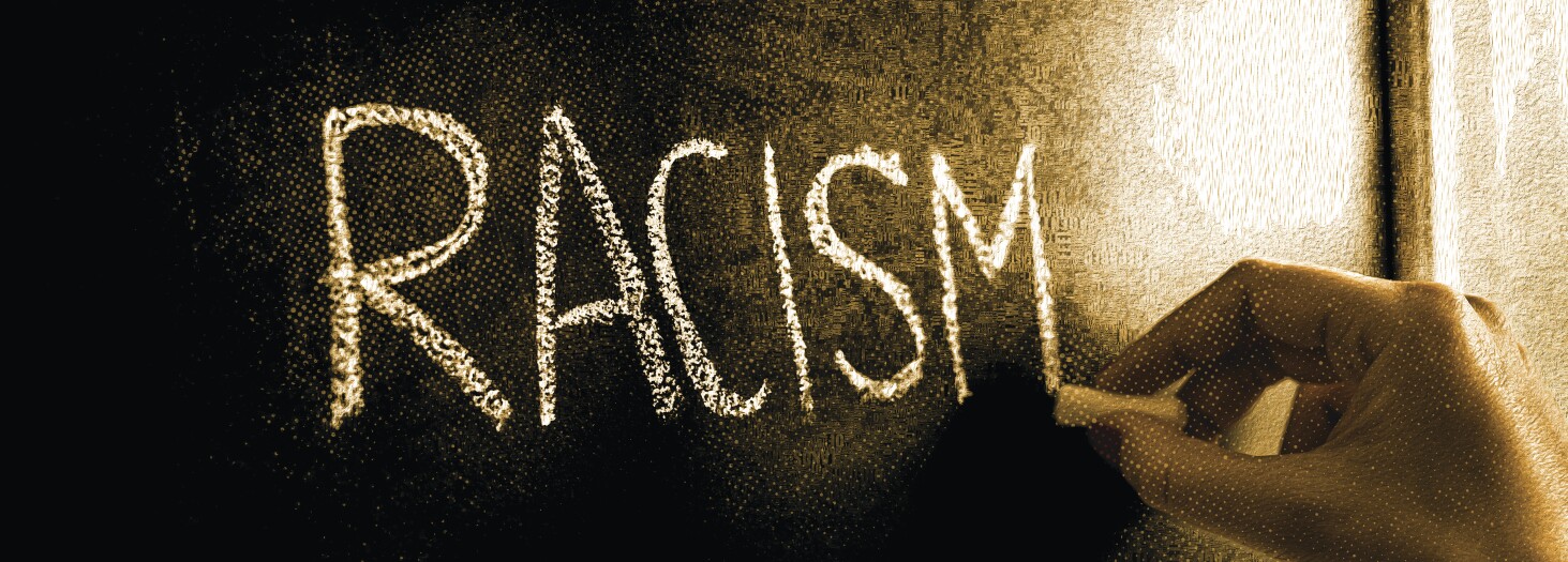 Hand writing the word racism on blackboard. Stop hate. Against prejudice and violence. Lecture about discrimination in school.