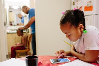 Kimora Gantt, right, does homework while her brother Jason Gantt, 5, gets his hair cut by his father, Bobby Gantt. After struggling with homelessness, the family has found stability in a home they rent through a local housing authority in Tacoma, Wash.