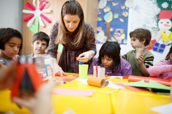 Special education teacher assisting a diverse group of elementary students in art class.