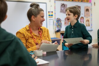 Art teacher Kesling St. Denis laughs with Wayne, 7, as they begin an activity decorating bunny masks during art class on March 30, 2023. The school works to incorporate topics the students are passionate about into the lessons.