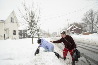 Rachel Grigsby tries to steady her daughter Mia Grigsby, 9, as she climbs over a snowbank, heading home from a trip to the corner store in Buffalo, N.Y., Friday, Nov. 18, 2022.