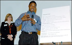 In Boston, mentor Carol Ball of Lehman Brothers supports 7th grader Solomon Bona during his presentation on financial terms.