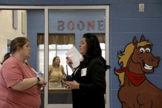 After directing students and parents in the pick-up line outside in 100 degree heat, principal Manuela Haberer fans herself as she speaks with her secretary, Laura Stiles, outside Boone Elementary School’s main office in San Antonio, Texas, on Thursday, May 19, 2022.