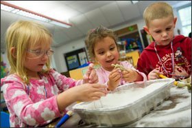 Preschoolers, from left, Eleanor Kimball, Thalia Lugo, and Sam Moschetto play paleontologist as they dig for dinosaurs buried in sand during class at Millville Elementary School. As part of the LEAP program used in the class, teachers encourage students to work and play collaboratively as much as possible.