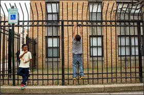 Dashawn Smith, 6, left, looks over at his friend Malachi Davis, 10, outside the Potomac Gardens public-housing complex in Washington. The fence was erected around the property to keep out drug dealers and other criminals. While the federal housing programs expanded through the War on Poverty provide stability for assisted families, their children still often live in concentrated poverty.
