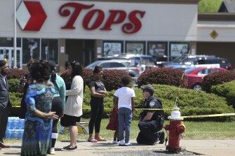 A Buffalo police officer talks to children at the scene of Saturday's shooting at a supermarket on Sunday, May 15, 2022, in Buffalo, N.Y. A white 18-year-old wearing military gear and livestreaming with a helmet camera opened fire with a rifle at the supermarket, killing and wounding people in what authorities described as “racially motivated violent extremism.”