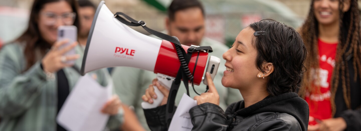 Young female demonstrator speaks to megaphone in front of bystanders