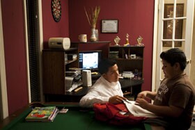 With an award for academic achievement hanging on the wall behind him, Angel Leon takes time out from his own schoolwork to help his brother with his studies at home.