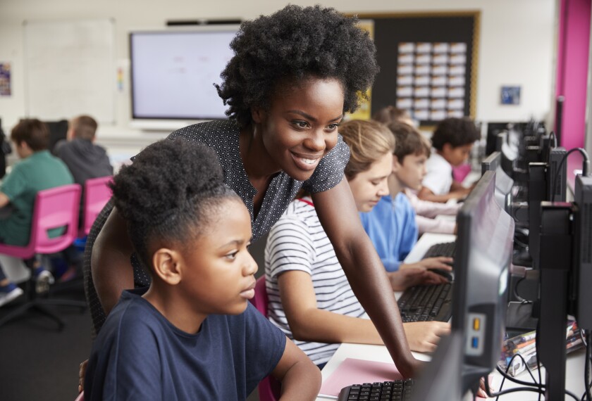 Teacher Helping Female Pupil Line Of High School Students Working at Screens In Computer Class