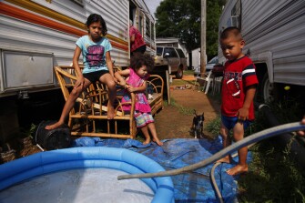 April Montemayor, 8, from left, her sister Berenise Montemayor, 2, and cousin Ruben Roblero, 4, wait for a pool to fill with water as ESL parent liaison Ida White visits her mom Maria Guerra inside their trailer in Foley, Ala. April is in first grade at Foley Elementary. Ms. White was trying to get the family to take advantage of summer learning programs.
