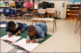 Isaiah Marshall, 7, in the plaid shirt, and Ugo Igwe, 6, use the floor, instead of desks and chairs, for workbook space at Robert Goddard Montessori School in Seabrook, Md.