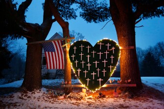 FILE - In this Dec. 14, 2013, file photo, a makeshift memorial with crosses for the victims of the Sandy Hook Elementary School shooting massacre stands outside a home on the first anniversary of the tragedy in Newtown, Conn. Five years later, residents are dealing with what it means to be from a place whose name has become synonymous with tragedy. Mary Ann Jacob, who was a school library clerk the day of the shooting and who became the chair of the town's legislative council in 2013, said "Some days it sits quietly by your side, and you acknowledge it and know it's there and move on with your day. Other days it's a really hard, difficult burden to bear."