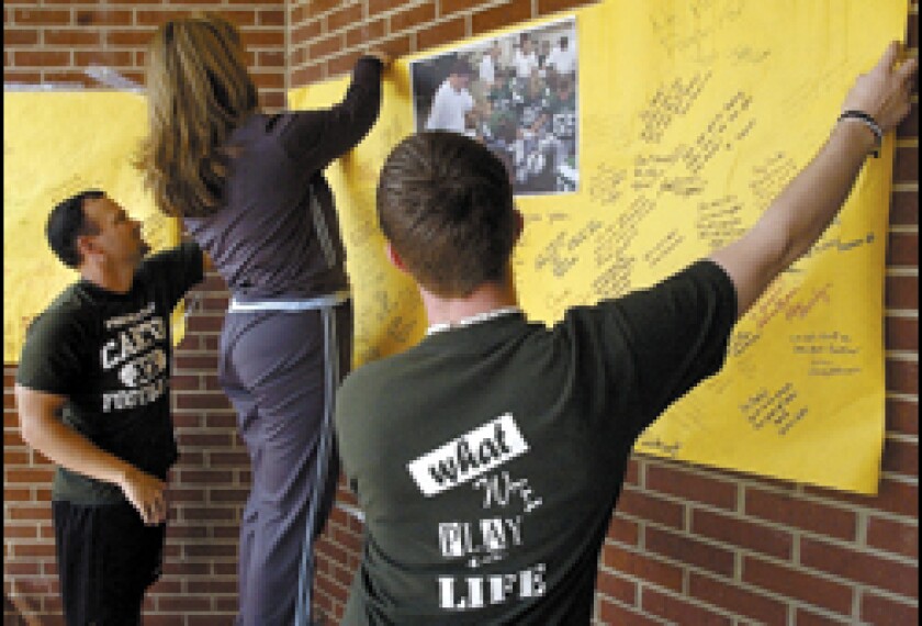 Canton High assistant football coach Howard Bell, far left, gets help hanging a poster for Gary Joe Kinne, the school's head football coach, who was hospitalized after being shot by a parent.
