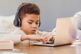 Young Black boy working on his laptop and wearing headphones.
