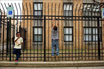 Dashawn Smith, 6, left, looks over at his friend Malachi Davis, 10, outside the Potomac Gardens public-housing complex in Washington. The fence was erected around the property to keep out drug dealers and other criminals. While the federal housing programs expanded through the War on Poverty provide stability for assisted families, their children still often live in concentrated poverty.