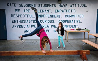 With the school motto emblazoned on the wall, Mia Keighan does a cartwheel on a balance beam while Angelena Resete looks on at Kate Sessions Elementary School in San Diego, Calif.