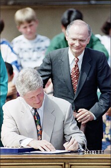 President Bill Clinton, under the watchful eye of Education Secretary Richard Riley, signs the Goals 2000 Educate America Act at the Zamorana Fine Arts Academy Elementary School in San Diego, Calif., on March 31, 1994.