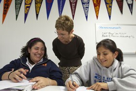 Teacher Merrily Brannigan works with Liliana Sofia Monsivais, left, Karla Acosta Lara, and Yasmine Aguirre, foreground, in a room festooned with college pennants.