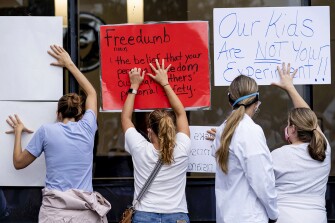 People in favor of a mask mandate for Cobb County schools hold signs against the window to the office during the school board meeting Thursday, Aug. 19, 2021, in Marietta, Ga.