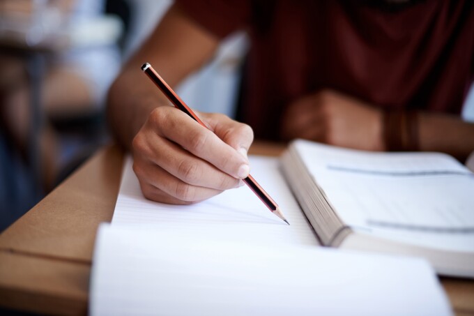 Image of a student writing on a notepad while looking at a textbook.