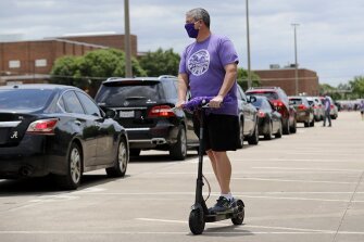 Chris Choat, principal at Richardson High School, rides a scooter past a long line of cars congratulating students on graduating in Richardson, Texas, on Friday, May 8, 2020. Choat said that the school graduated 631 seniors this year and he and his staff greeted all those who drove up to collect their caps and gowns.