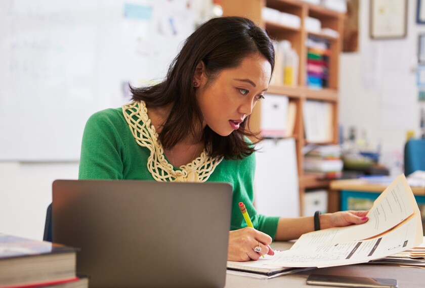 Female Asian teacher at her desk marking students' work