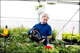 In nearby Sheboygan Falls, 11th grader Dylan Thiel waters plants in one of the newly constructed “hoop houses,” or greenhouses, at Sheboygan Falls High School.