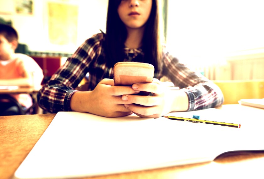 Close up of elementary or middle school white girl using a mobile phone in the classroom.