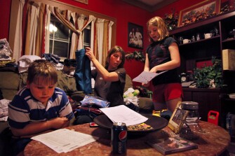 Ronnie Auville, 7, left, works on homework while his mom, Julia, checks the "musical alphabet" his sister Emily, 9, did during school in their McDowell County home. Three of the four Auville family children attend Iaeger Elementary School.