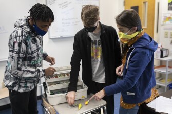 Megan Bowen shows examples of 3D printed fishing lures to Salem Academy Charter School students Marcus Marie and Camden Grinarml during class in Salem, Mass., on April 25, 2022.