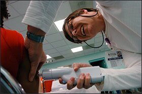 Beth Amstad, a registered nurse at the Southeastern Health Center, uses a compressed air device to vaccinate a student.