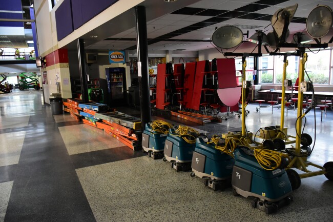 Ladders, cleaning machines, and high-powered lights are lined up outside a cafeteria in the educational complex.