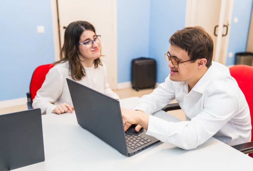 Teacher helping adult special-needs student with computer.